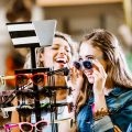 Zwei Teenagerinnen kaufen sich von ihrem Jugendlohn eine Sonnenbrille.