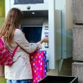 Kind hebt digital ausbezahltes Taschengeld von Bankautomaten ab.