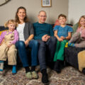 Familie sitzt gemeinsam auf Sofa.