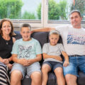 Eine Familie mit Vater, Mutter und zwei Söhnen im Schulalter sitzt auf dem Sofa