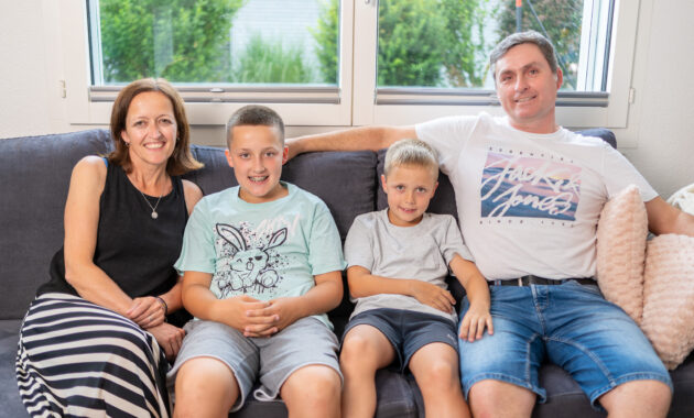 Eine Familie mit Vater, Mutter und zwei Söhnen im Schulalter sitzt auf dem Sofa
