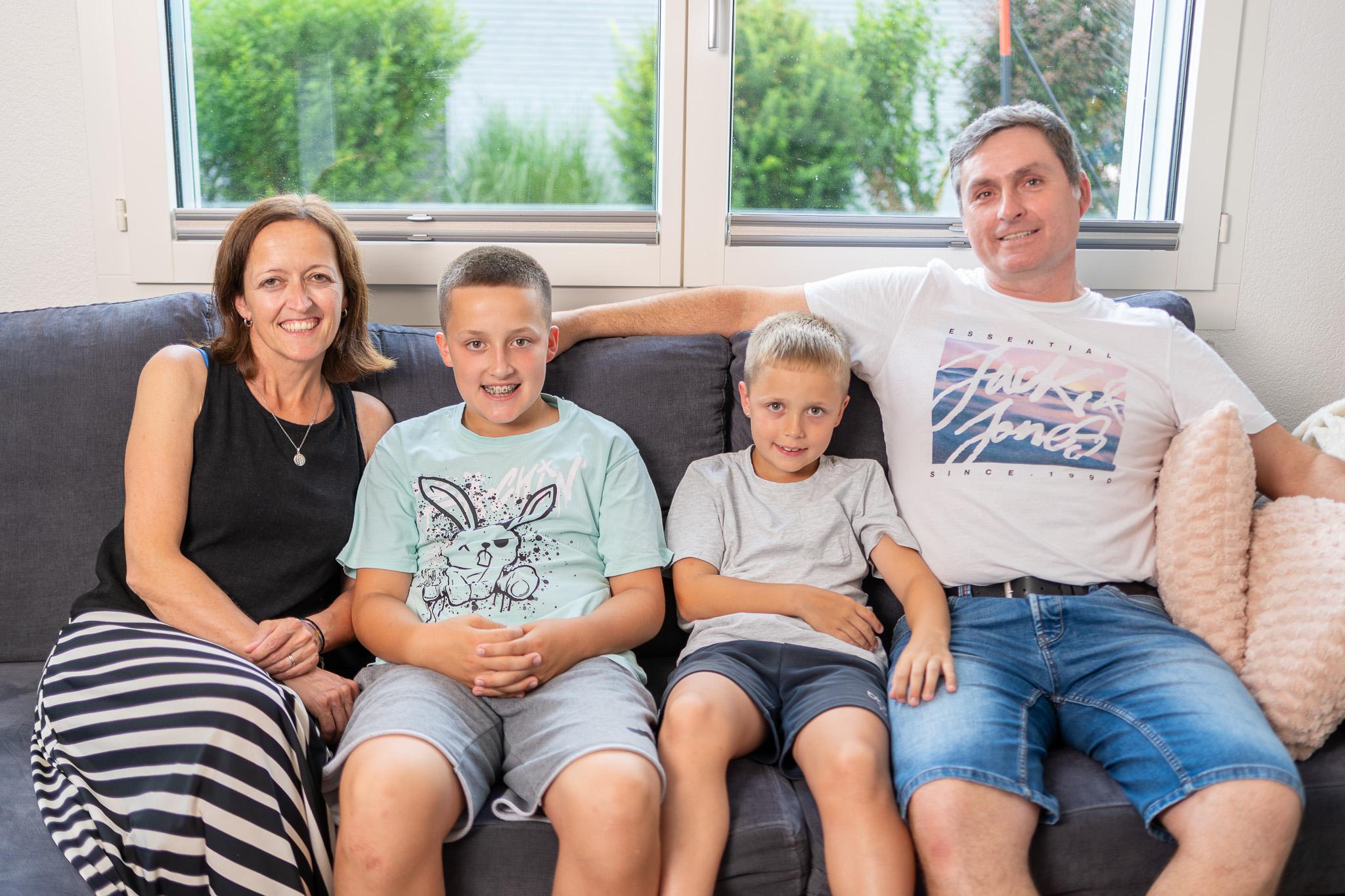 Eine Familie mit Vater, Mutter und zwei Söhnen im Schulalter sitzt auf dem Sofa