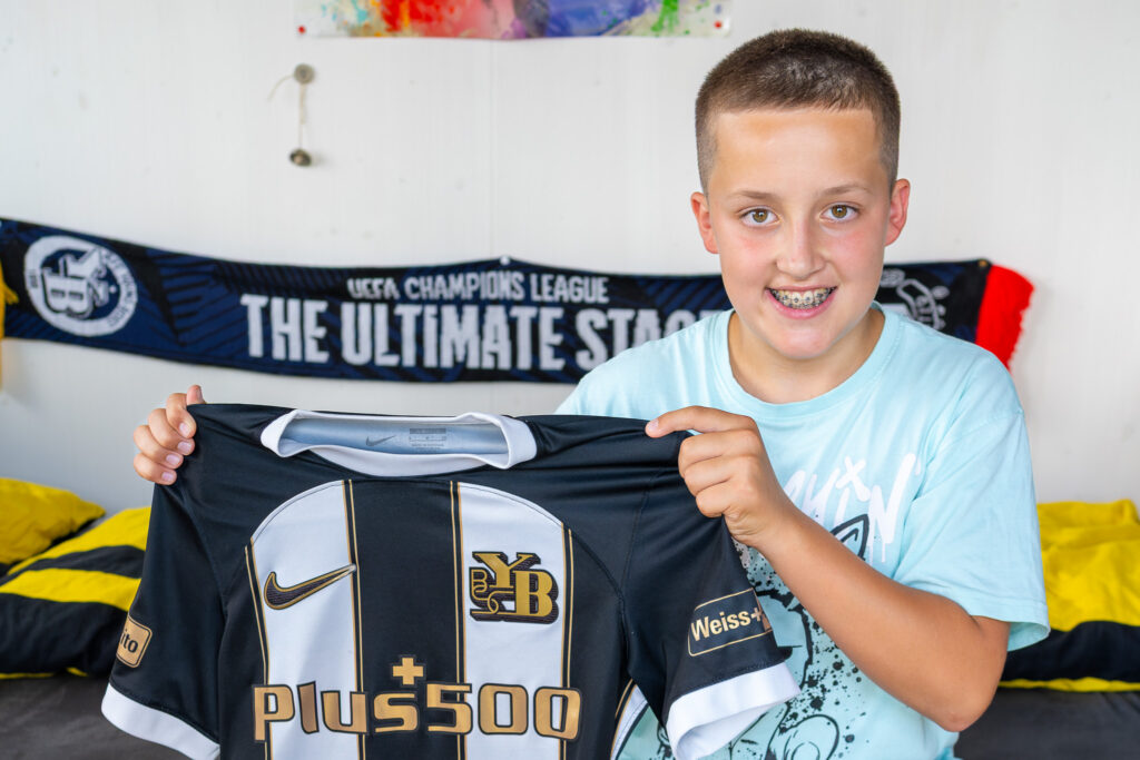Ein Junge hält mit beiden Händen ein Fussballshirt hoch.