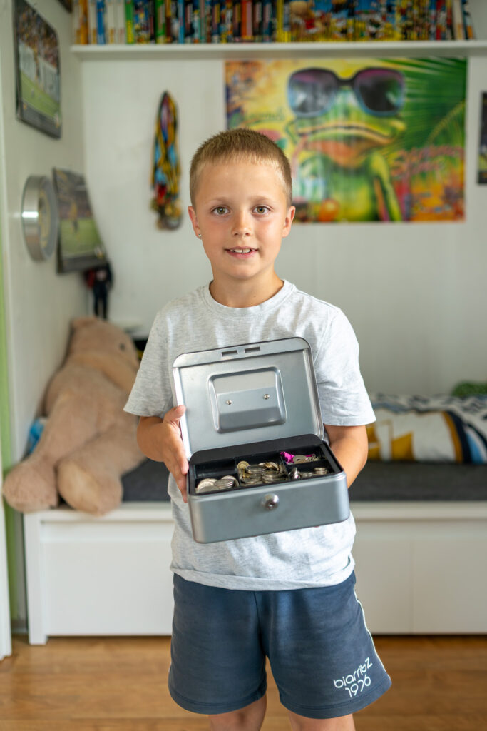 Bub mit offener Geldkassette mit Münzfächern.